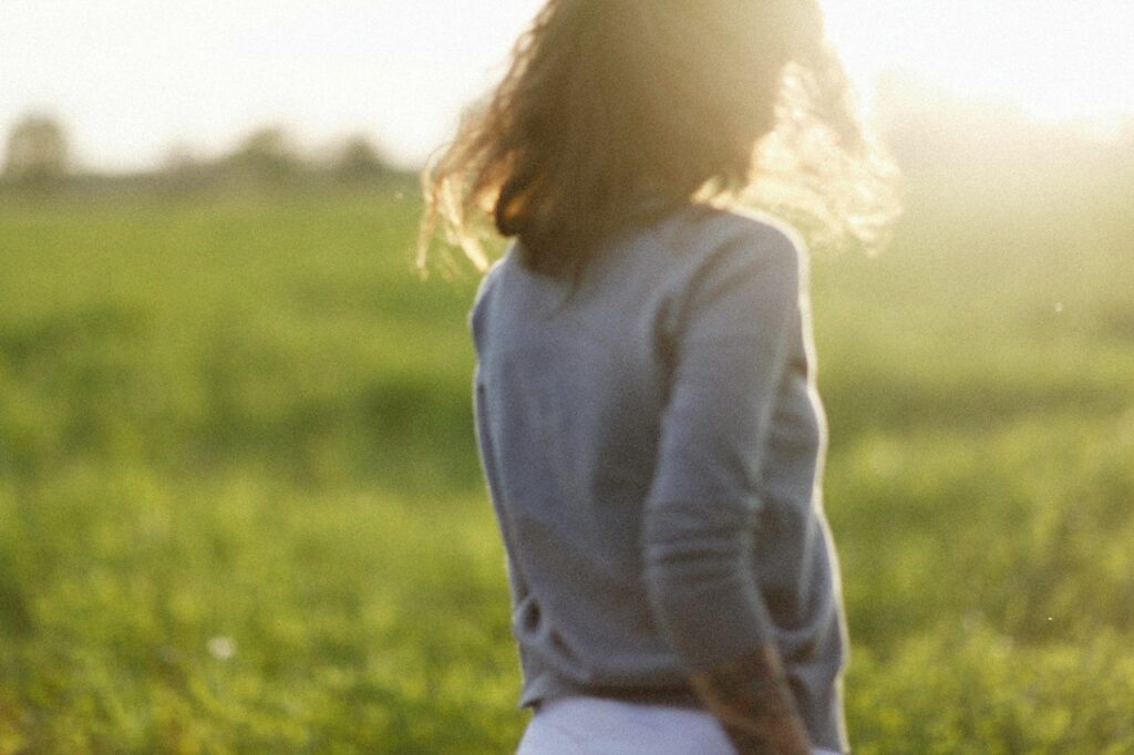 Artistic depiction of a woman standing in a sunlit field with a blurred effect.